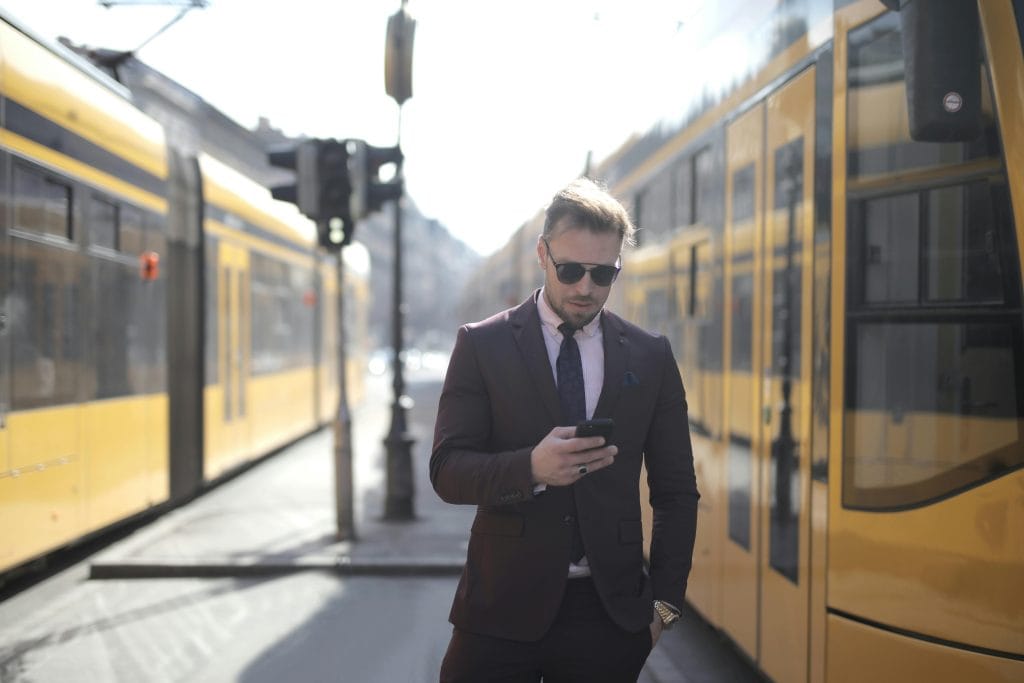 Persona vestida de traje de oficina entre dos trenes mirando el móvil