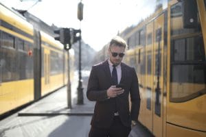 Persona vestida de traje de oficina entre dos trenes mirando el móvil
